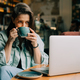 Working freelancer woman drinking coffee in a coffee shop and using a laptop. - PhotoDune Item for Sale