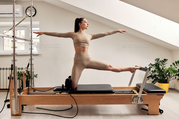 A young girl is doing Pilates on a reformer bed. A beautiful