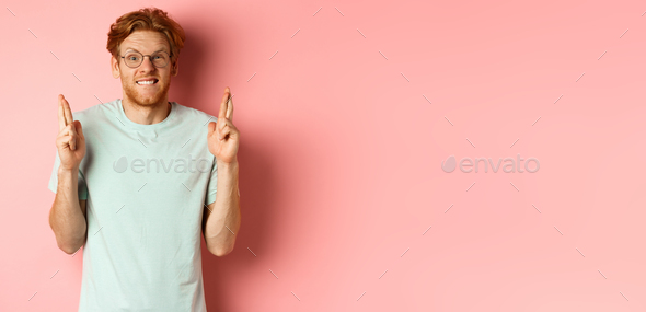Worried redhead man waiting for results, expecting something with fingers crossed, biting finger