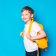 Schoolboy with yellow backpack stands sideways against blue background - PhotoDune Item for Sale