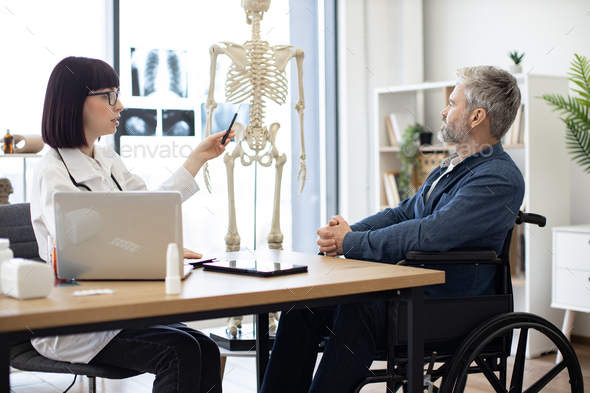 Female doctor talking to male in wheelchair using skeleton - Stock Photo - Images