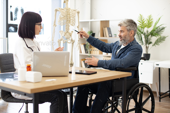 Female doctor talking to male in wheelchair using skeleton - Stock Photo - Images