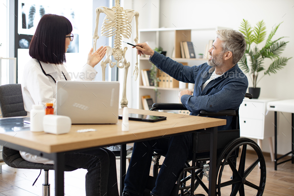 Physician and man with disability examining skeleton model - Stock Photo - Images