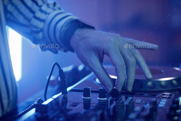 Closeup of male DJ adjusting switches at turntable in neon lights at disco party
