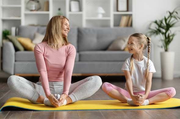 Foto de Little girl doing stretching exercises, practicing yoga on fitness  mat at home do Stock