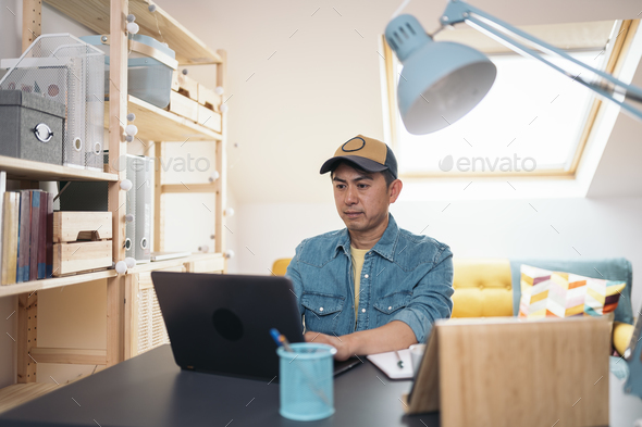 Asian man using laptop while working in a home office - Stock Photo - Images