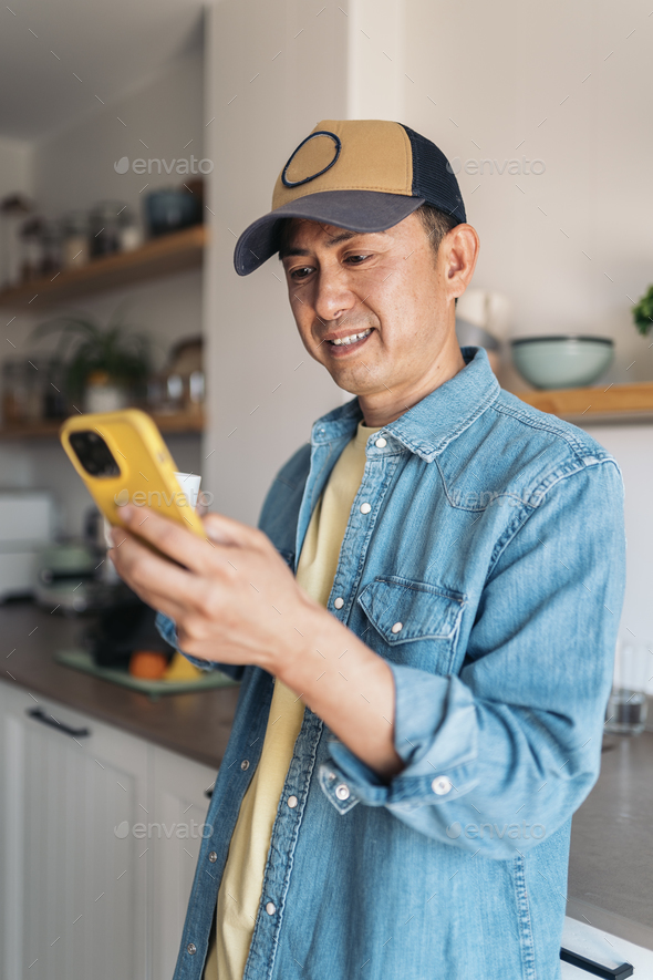 Asian man drinking coffee and using mobile at home - Stock Photo - Images