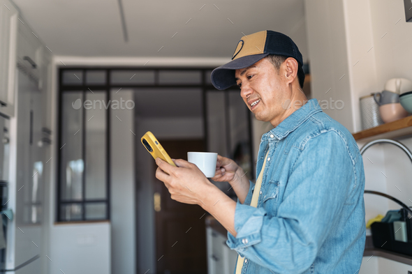 Asian man drinking coffee and using mobile at home - Stock Photo - Images
