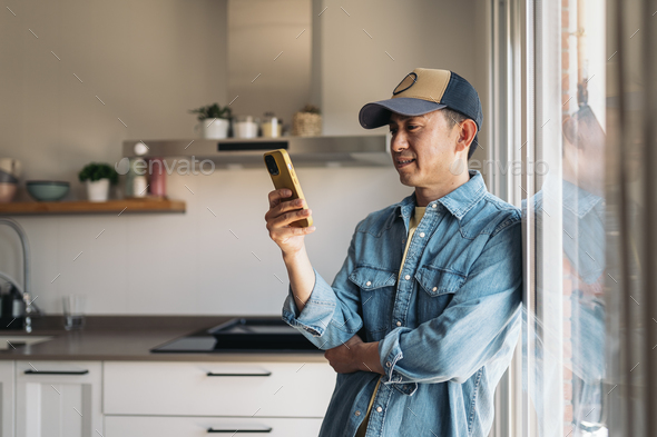 Asian man using mobile standing at home - Stock Photo - Images