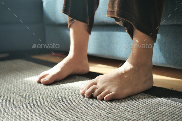 Woman sitting on sofa with feet on carpet at home. - Stock Photo - Images