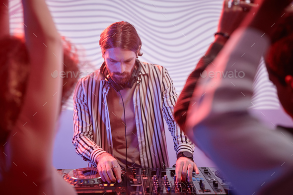 DJ by turntable in neon lights with dancing crowd in nightclub - Stock Photo - Images