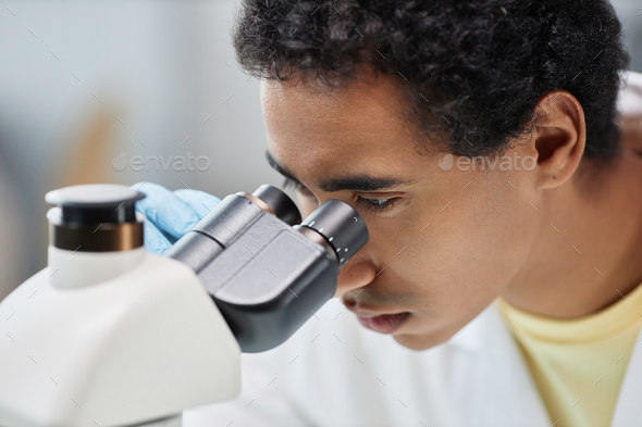 Ethnic man as scientist looking in microscope in laboratory - Stock Photo - Images