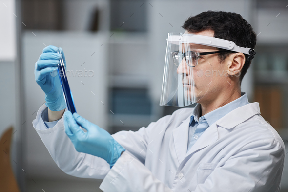 Scientist wearing face shield in laboratory doing experiments with test tube - Stock Photo - Images