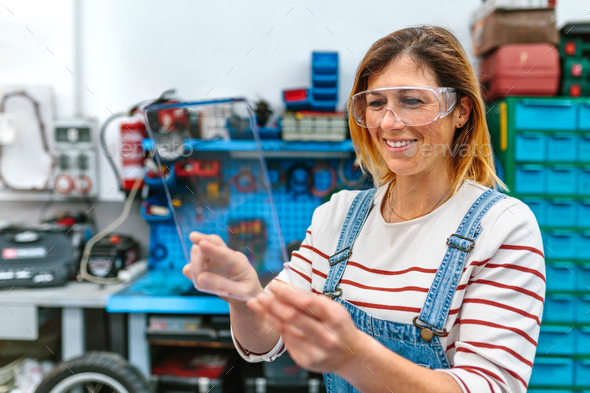Female mechanic with security glasses touching transparent tablet - Stock Photo - Images