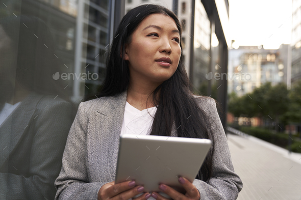 Business Chinese woman standing next to the building and holding digital tablet - Stock Photo - Images
