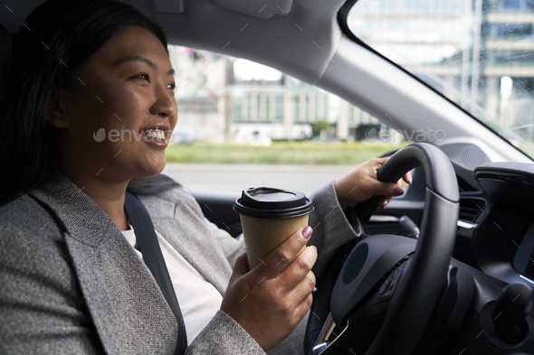 Chinese woman driving a car and holding a cup of coffee - Stock Photo - Images