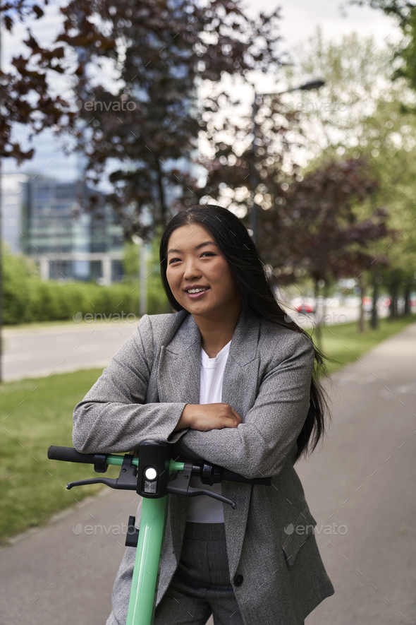 Portrait of Chinese woman riding on electric scooter in business outfit - Stock Photo - Images