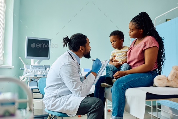 Black pediatrician talking to small boy and his mother at doctor's office. - Stock Photo - Images