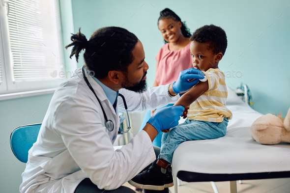 Small black boy about to get vaccinated by pediatrician at doctor's office. - Stock Photo - Images
