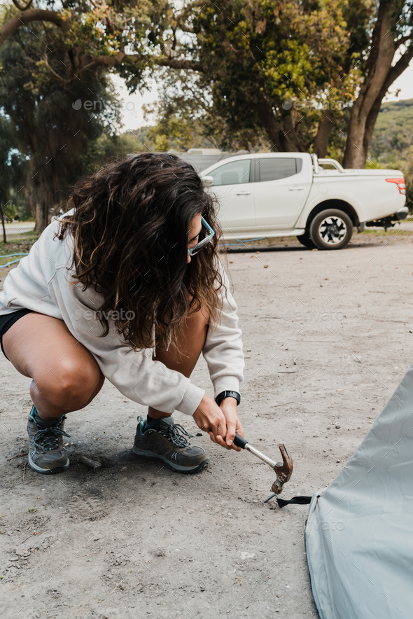 Female backpacker put up a tent with hammer and stakes in the woods