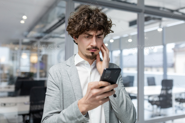 Businessman in office near window upset reading message online notification from phone, male boss