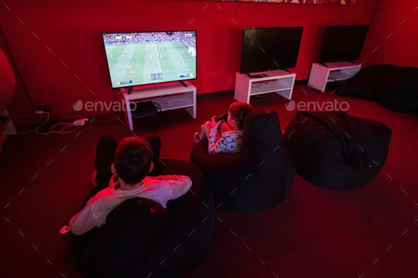 Two boys gamers play football gamepad video game console in red gaming room. - Stock Photo - Images