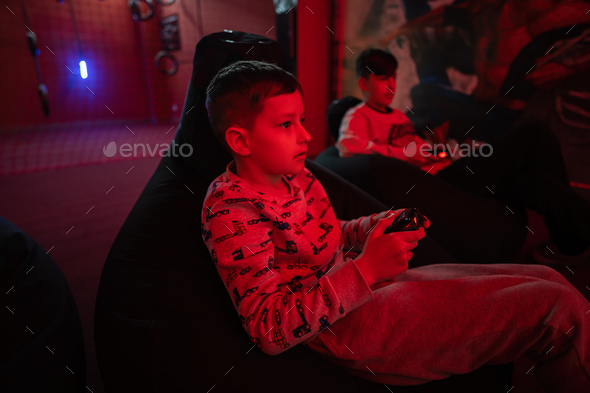 Two boys gamers play gamepad video game console in red gaming room.