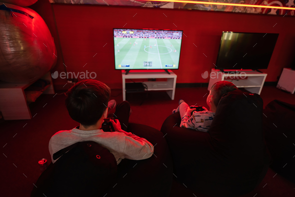 Two boys gamers play football gamepad video game console in red gaming room. - Stock Photo - Images
