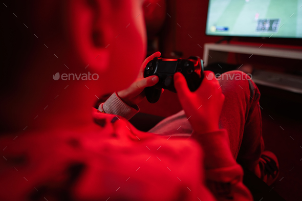 Boy gamer play gamepad football video game console in red gaming room. - Stock Photo - Images
