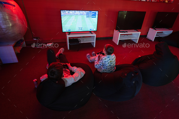 Two boys gamers play gamepad video game console in red gaming room.