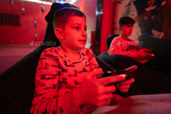 Two boys gamers play gamepad video game console in red gaming room. - Stock Photo - Images