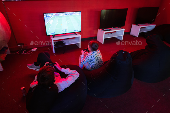 Two boys gamers play football gamepad video game console in red gaming room.
