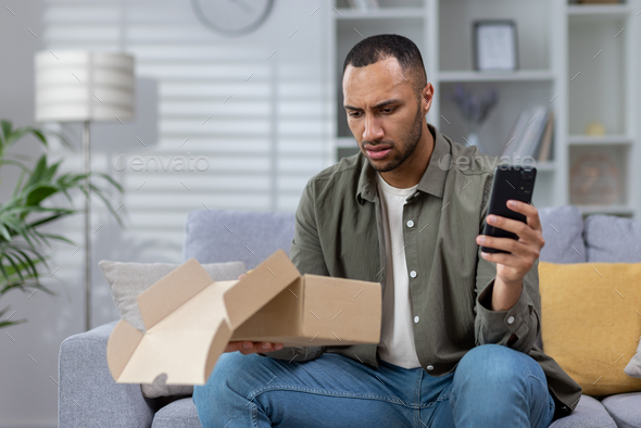 A worried young Hispanic man received a wrong and damaged package, an online store order, at home