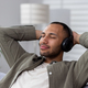 Smiling and relaxed hispanic man relaxing at home on sofa wearing headphones, listening to music - PhotoDune Item for Sale