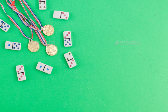 White dominoes with colorful dots and winner medals on a green background, top view. Board game.