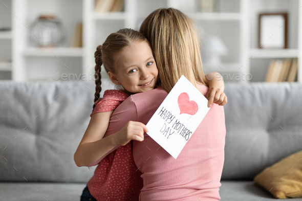 Cute Little Girl Holding Handmade Greeting Card And Embracing Mom At Home - Stock Photo - Images