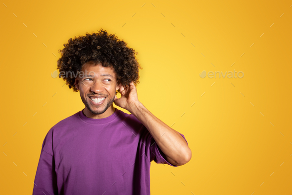 Happy pensive mature black curly man in violet t-shirt thinking and scratching head - Stock Photo - Images