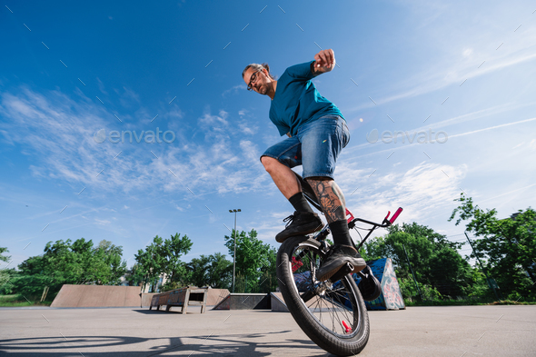 Full length of a skilled mature tattooed man balancing on one wheel on his bmx in a skate park.