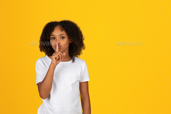Happy mysterious adolescent curly girl in white t-shirt making shh gesture, secret sign - Stock Photo - Images