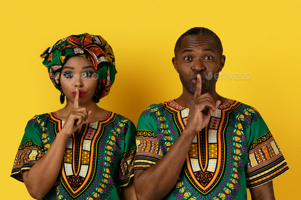 Beautiful black couple in african costumes showing silence gesture - Stock Photo - Images
