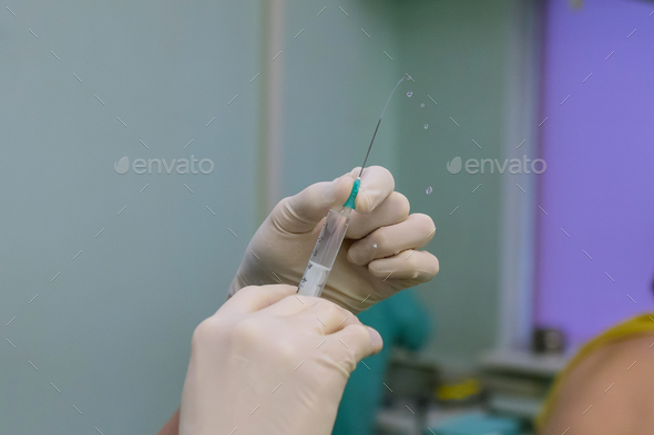 Doctor fills syringe with medication while preparing to administer it to patient during treatment - Stock Photo - Images