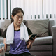 Asian woman playing smartphone at home during break from yoga exercise and drinking fresh water. - PhotoDune Item for Sale