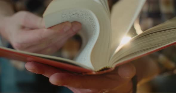 Close-up, Hands Are Flipping an Old Book and Dust From It Is Flying To the Light. A Beautiful Girl alt