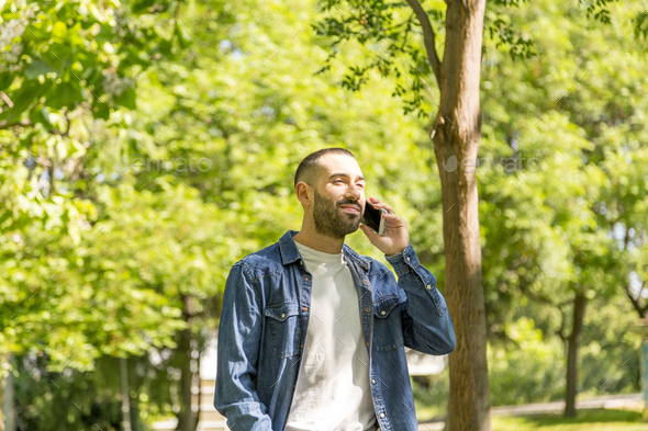Young man talking on phone while walking in a park. - Stock Photo - Images