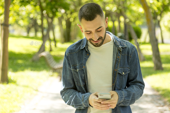 Young man texting while taking a walk in a park - Stock Photo - Images