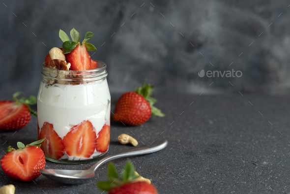 Greek yogurt, nuts and strawberries in a glass jar on grey table with a spoon close up, copy space - Stock Photo - Images