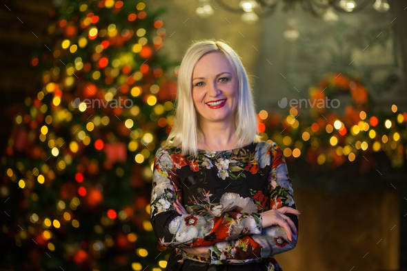 Woman is standing by fireplace against background of the Christmas tree