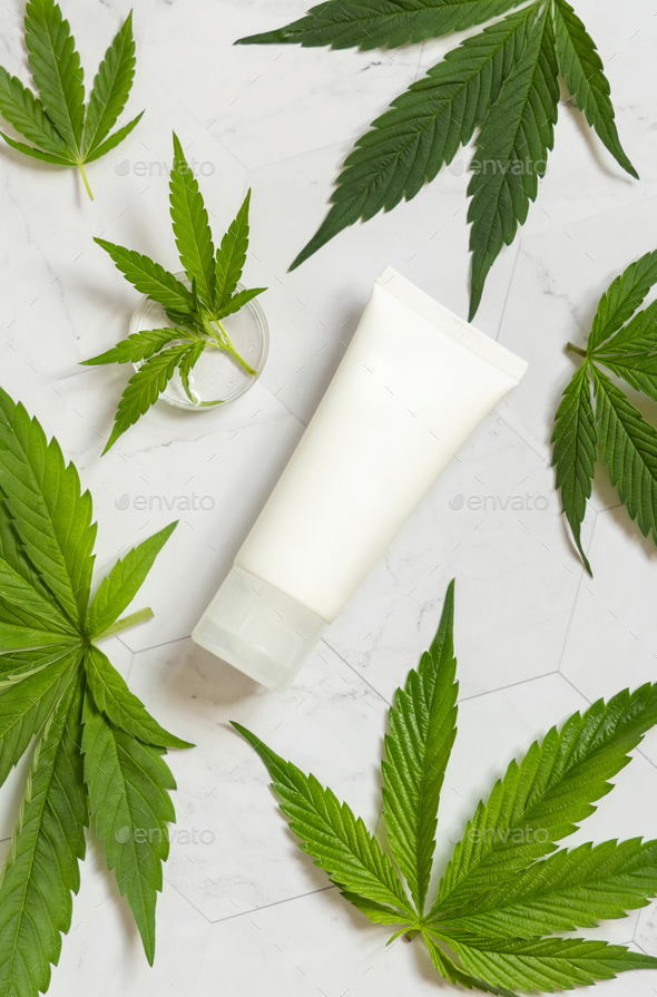 Blank Cream tube near green cannabis leaves on white table, top view. Cosmetic Mockup - Stock Photo - Images