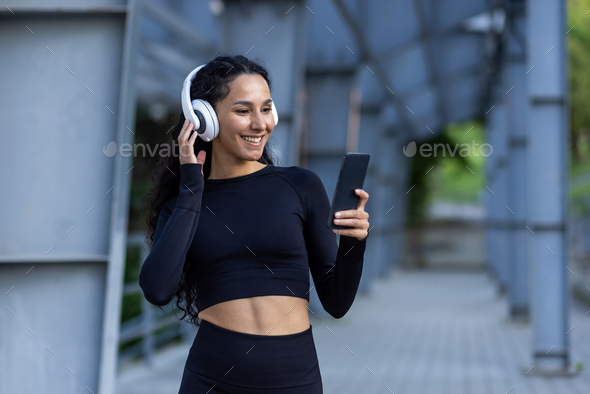 Hispanic sportswoman with headphones listening to online music and audio podcasts with books while - Stock Photo - Images