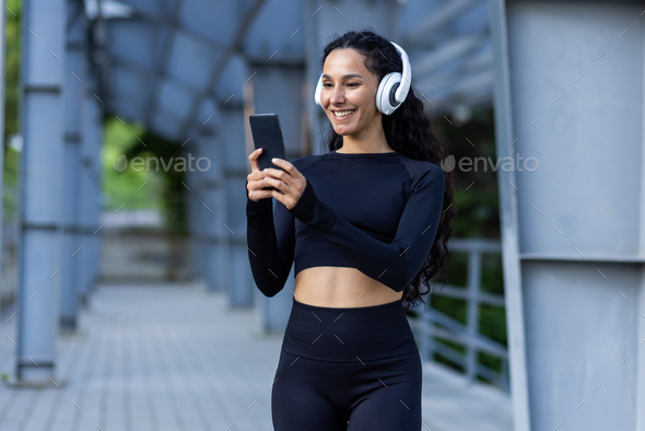 Hispanic sportswoman with headphones listening to online music and audio podcasts with books while - Stock Photo - Images